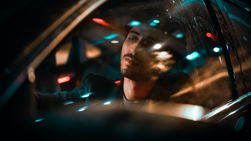 Man driving at night reflected in car window with colorful bokeh lights
