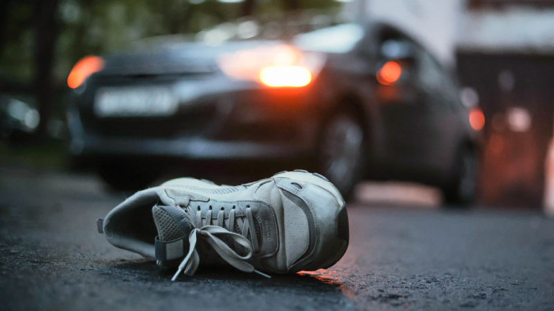 Shoe on asphalt with car in background after car accident.