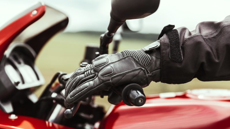 A human hand in protective motorcycle gloves holds a motorcycle, presses the brake before the race, close-up
