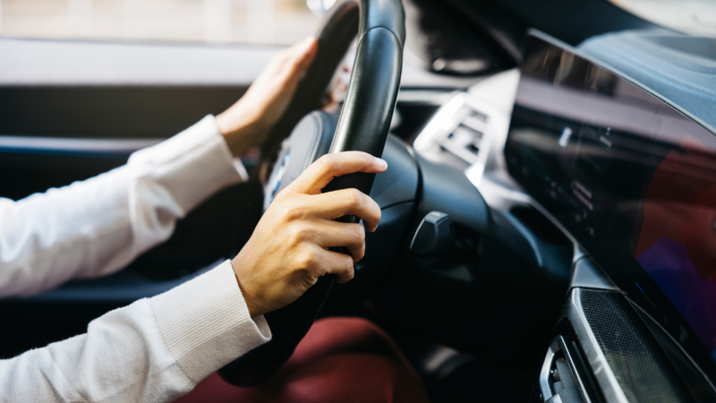 Close-up of a person's hands holding the steering wheel of an electric car, showcasing modern technology and eco-friendly automotive design.