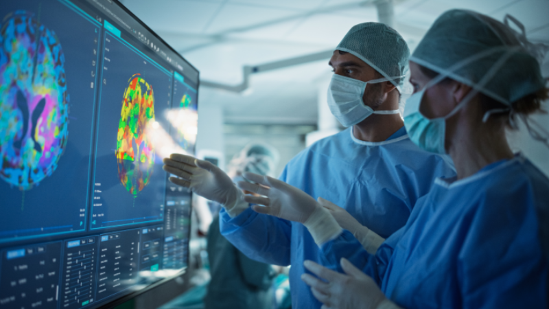 Before Beginning the Surgery, Female Lead Surgeon and an Assistant Looking at Detailed Brain PET Scans on a Large Computer Screen, Making Key Decisions Together with the Team