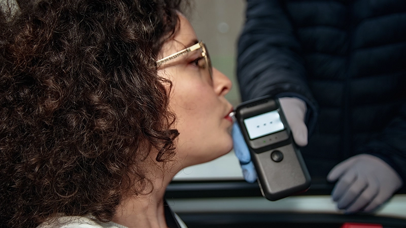 Woman undergoing breathalyzer alcohol test at a roadside traffic stop by police.