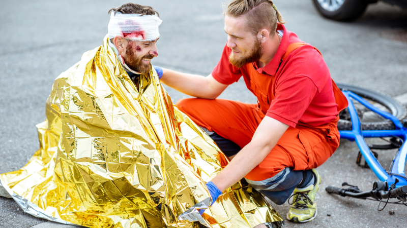 Ambluence worker covering injured man with thermal blanket, providing emergency care after the road accident