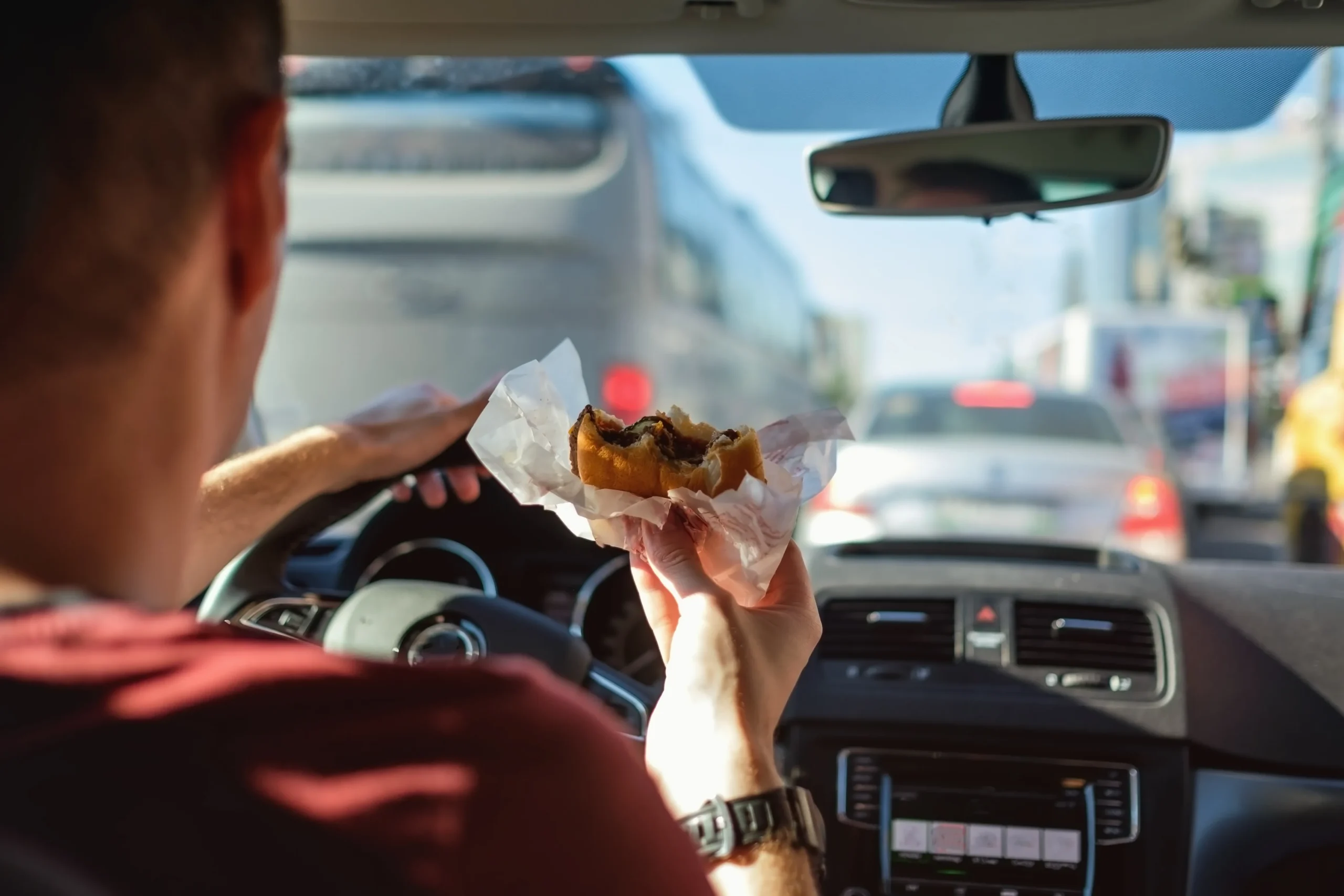 Man driving car while eating burger.