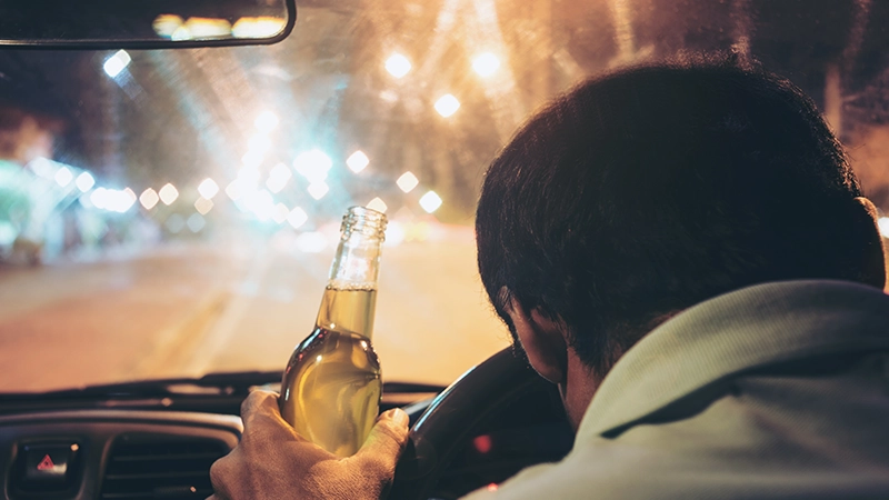 Drunk young man drives a car with a bottle of beer.