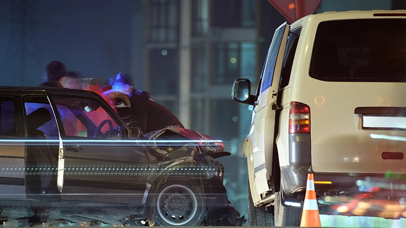 Nighttime city car crash site with heavily damaged vehicles and silhouettes of people.