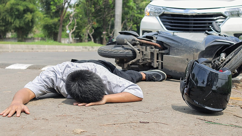 Motorcycle accident scene with man injured and lying on road.