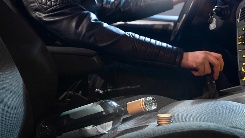 Drunk young man driving with an empty wine bottle.