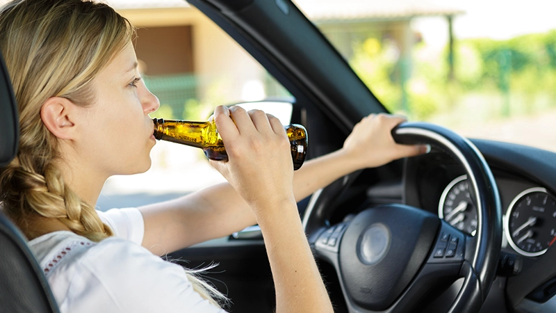 Woman drinking from a beer bottle while driving car.