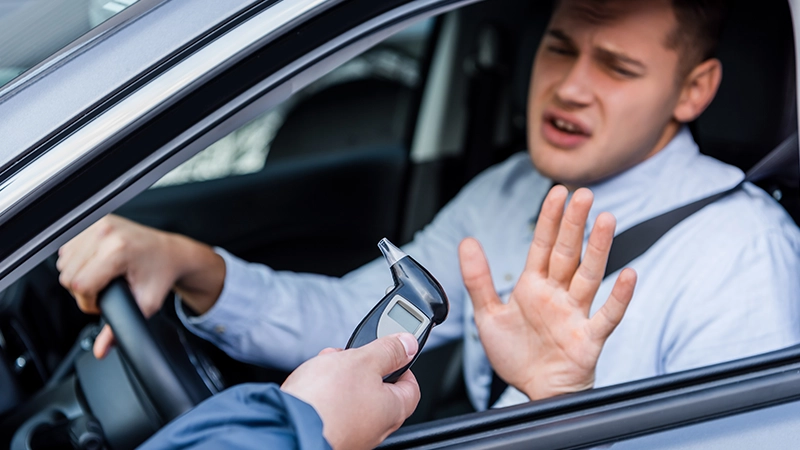 Policeman giving breathalyzer to drunk driver showing refuse gesture.