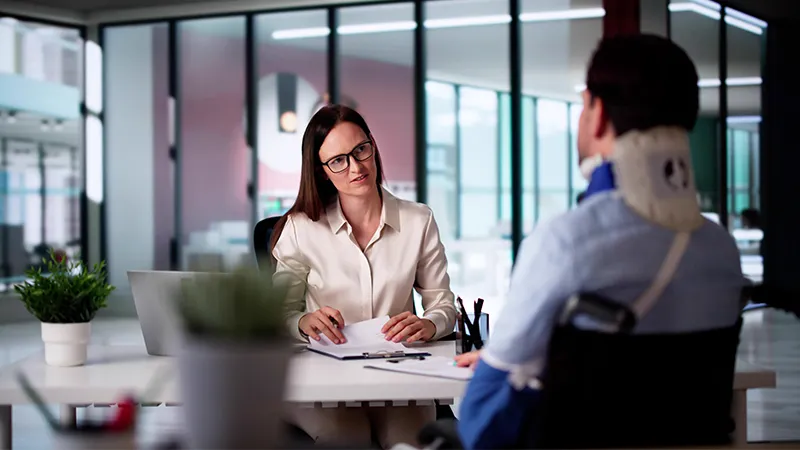 A female lawyer at a desk listening to an injured client in a wheelchair.