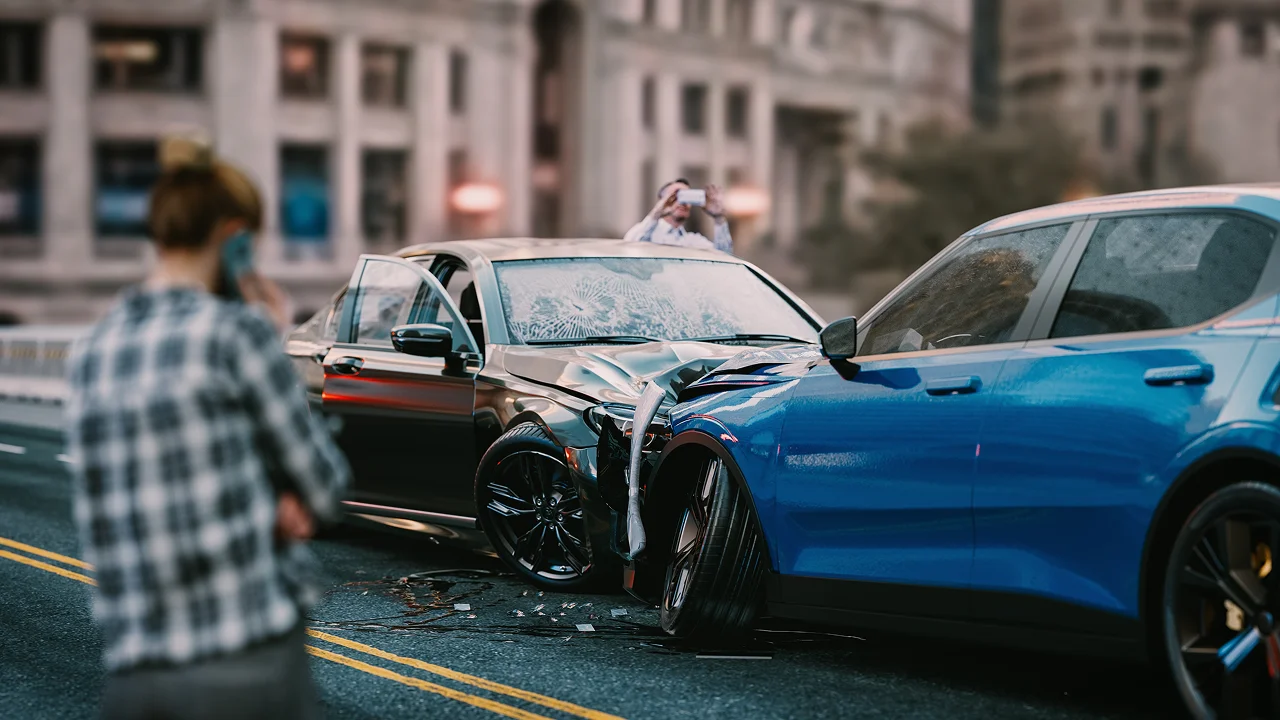 a person in a plaid shirt stands in the foreground, looking toward a fresh two-car collision between a blue SUV and a dark sedan on a city street.