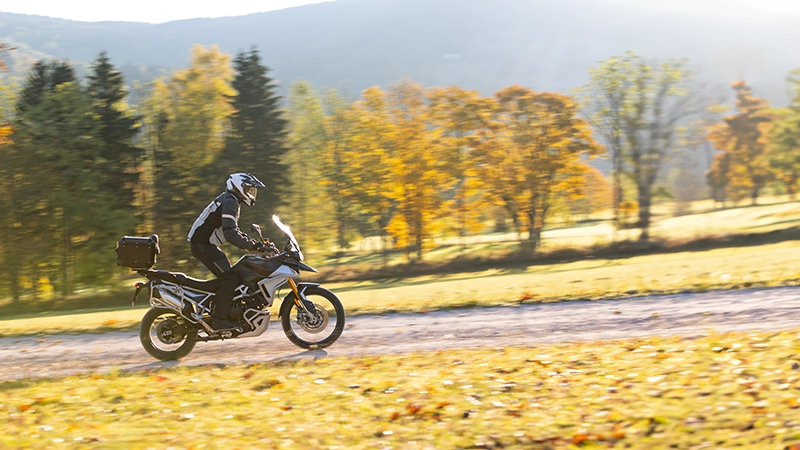 Driver riding motorcycle on empty road during sunset, autumn mountains.