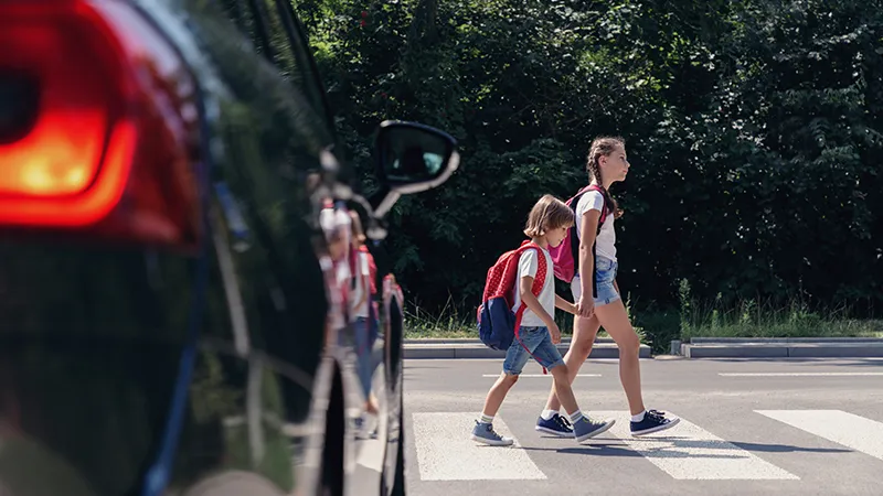 Children next to a car walking through pedestrian crossing to the school.