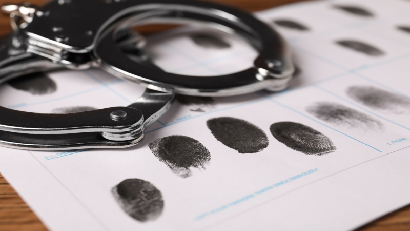 Paper sheet with human fingerprints and handcuffs on table, closeup. Criminal conviction