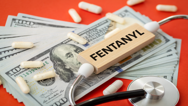 Fentanyl. Medical concept. Problem of drug addiction and drug trafficking. Word Fentanyl on a wooden block a stack of dollars, capsules, a medical stethoscope. Red background