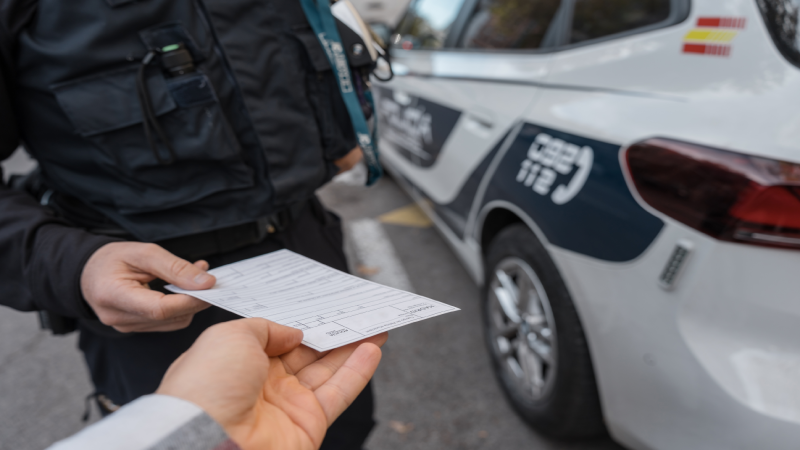 Police officer handing over a document to a driver near a patrol car during a roadside check