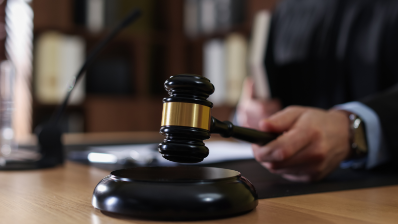 Judge striking gavel at wooden table indoors, selective focus